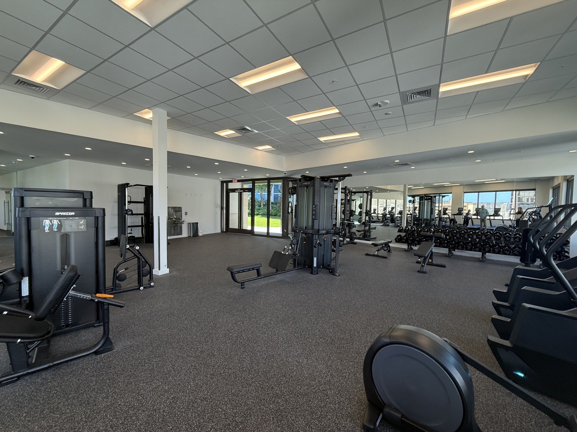 A spacious gym with various exercise equipment and a large mirror on the wall.